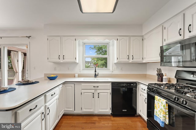 kitchen with black appliances, a sink, a peninsula, white cabinetry, and light wood-style floors