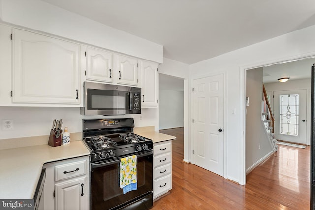 kitchen with stainless steel microwave, black gas stove, light wood finished floors, and white cabinets