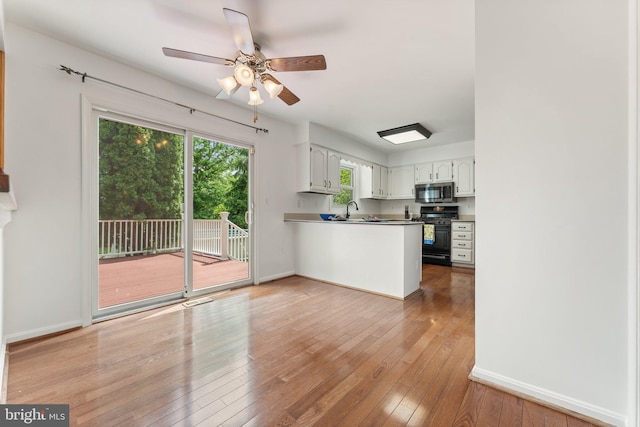 kitchen featuring black range with gas cooktop, stainless steel microwave, a peninsula, ceiling fan, and light wood-style floors