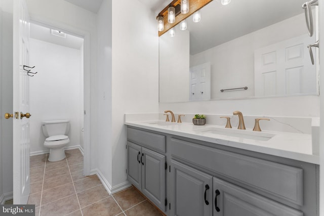 full bath with toilet, tile patterned floors, double vanity, and baseboards