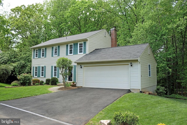 colonial home featuring asphalt driveway, a chimney, a front yard, and an attached garage