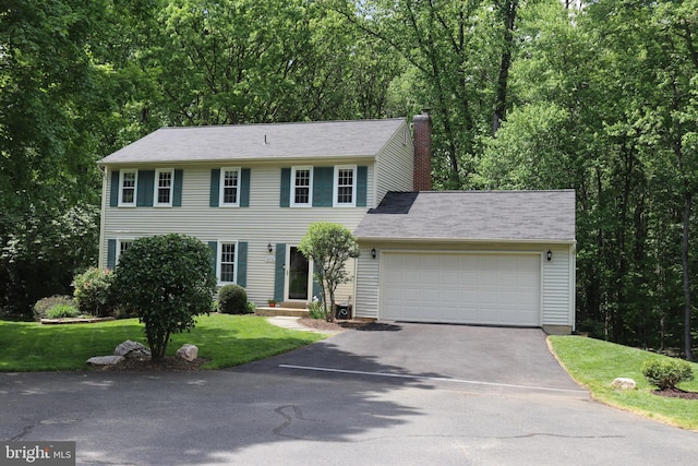 colonial home featuring driveway, a chimney, a front yard, and an attached garage