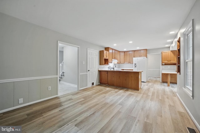 kitchen featuring white fridge with ice dispenser, a peninsula, light wood-style flooring, light countertops, and open floor plan
