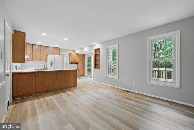 kitchen featuring white fridge with ice dispenser, a peninsula, light wood-style floors, light countertops, and baseboards