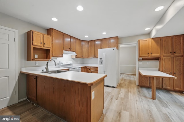 kitchen featuring white appliances, a sink, under cabinet range hood, a peninsula, and light wood-style flooring