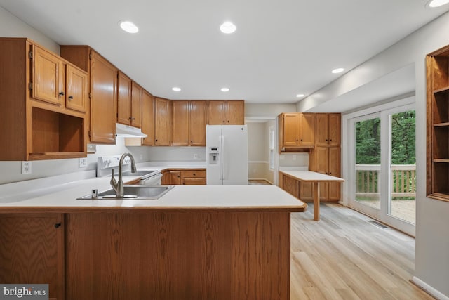 kitchen with white appliances, under cabinet range hood, a peninsula, light wood finished floors, and a sink