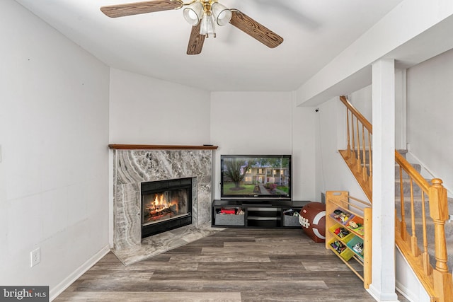 living area with stairway, a fireplace, a ceiling fan, and wood finished floors