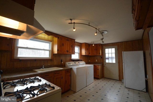 kitchen featuring wood walls, washing machine and dryer, white appliances, brown cabinets, and a sink