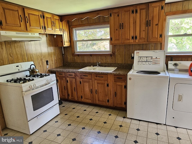 kitchen with independent washer and dryer, a sink, wood walls, white range with gas stovetop, and under cabinet range hood
