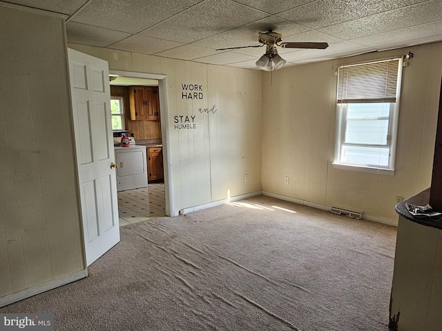 spare room with a ceiling fan, light colored carpet, visible vents, wood walls, and washer / dryer