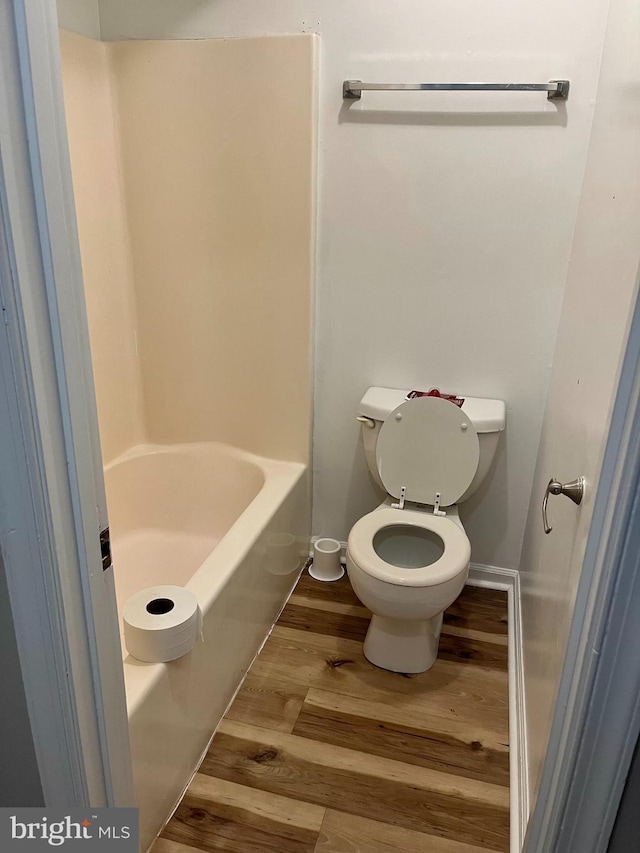 bathroom with a shower, wood finished floors, toilet, a washtub, and baseboards