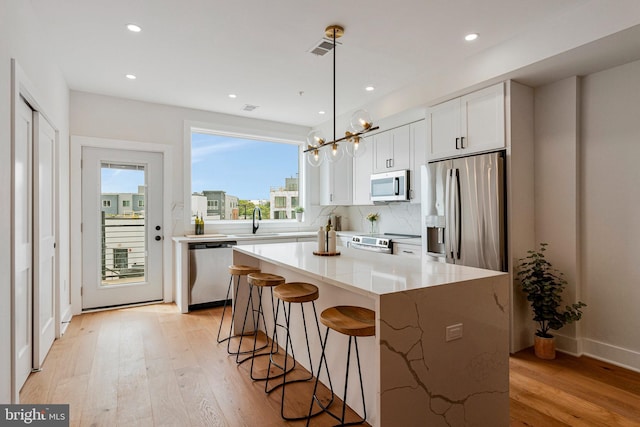 kitchen featuring a breakfast bar area, white cabinets, a sink, light wood finished floors, and stainless steel appliances
