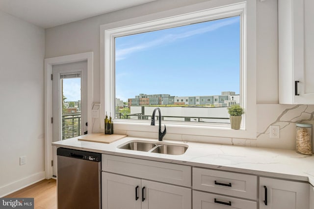 kitchen featuring light stone counters, a sink, light wood-style flooring, baseboards, and stainless steel dishwasher
