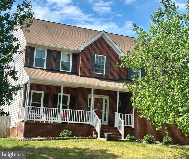view of front of house with covered porch, brick siding, a shingled roof, and a front lawn