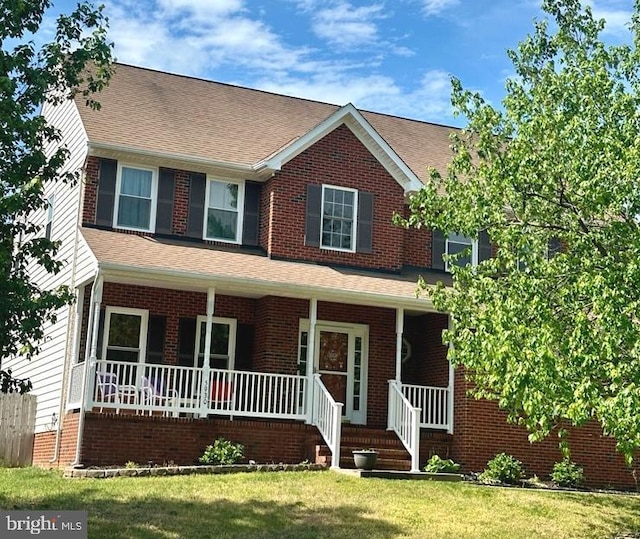 view of front of house with covered porch, brick siding, a shingled roof, and a front lawn