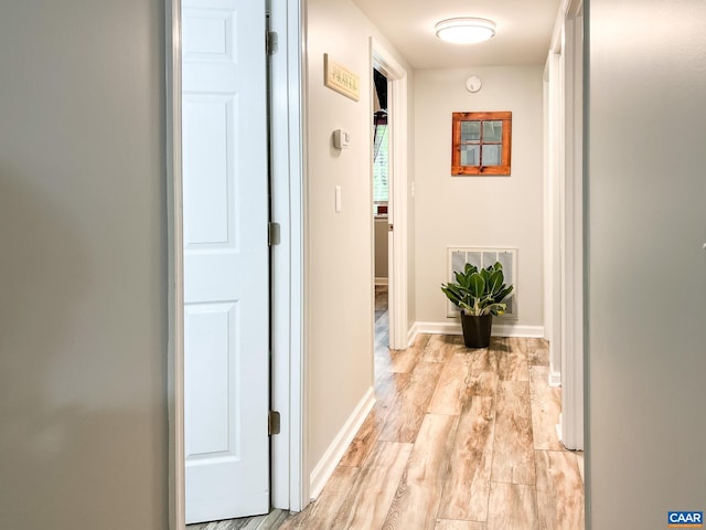 hall with baseboards, light wood finished floors, and visible vents