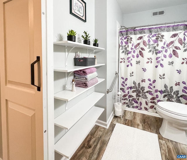 bathroom featuring a shower with curtain, toilet, wood finished floors, and visible vents