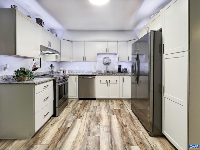 kitchen featuring under cabinet range hood, white cabinets, a sink, light wood finished floors, and appliances with stainless steel finishes