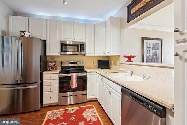 kitchen featuring stainless steel appliances, light countertops, a sink, wood finished floors, and white cabinetry