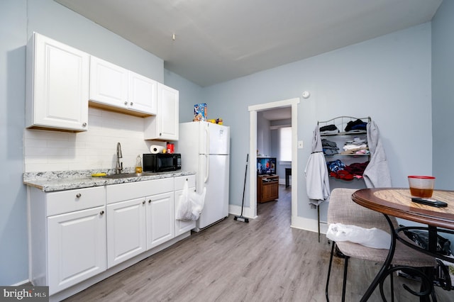 kitchen with freestanding refrigerator, white cabinetry, black microwave, tasteful backsplash, and light wood-type flooring