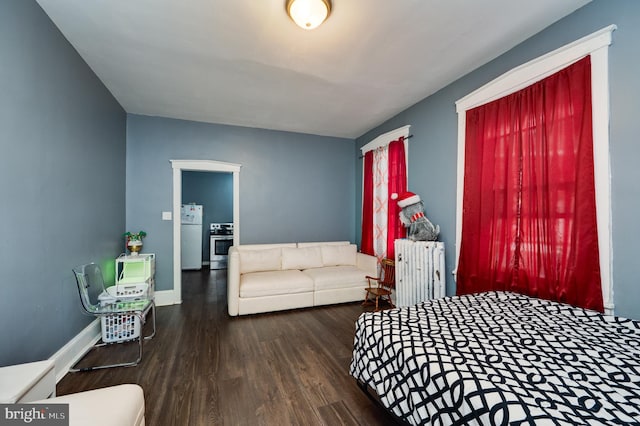 bedroom featuring freestanding refrigerator, radiator, baseboards, and wood finished floors
