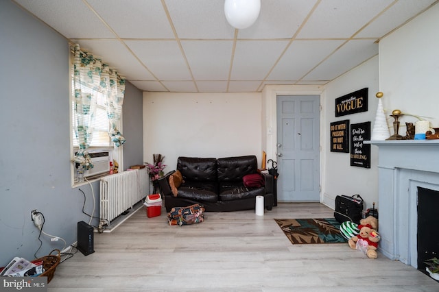 living room featuring wood finished floors, radiator heating unit, a fireplace, cooling unit, and a drop ceiling