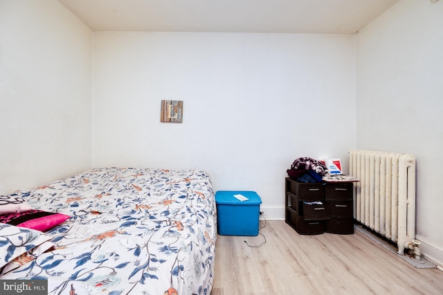 bedroom with radiator, wood finished floors, and baseboards