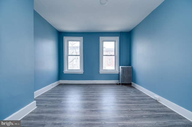 spare room featuring baseboards, radiator heating unit, and dark wood-type flooring