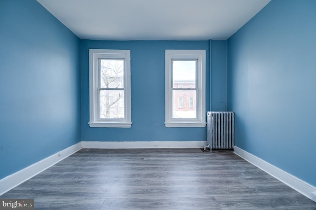 unfurnished room featuring radiator, baseboards, and dark wood-type flooring