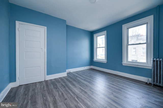 empty room with radiator, baseboards, and dark wood-type flooring