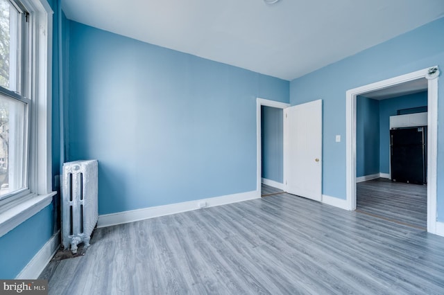 interior space featuring freestanding refrigerator, radiator, baseboards, and wood finished floors