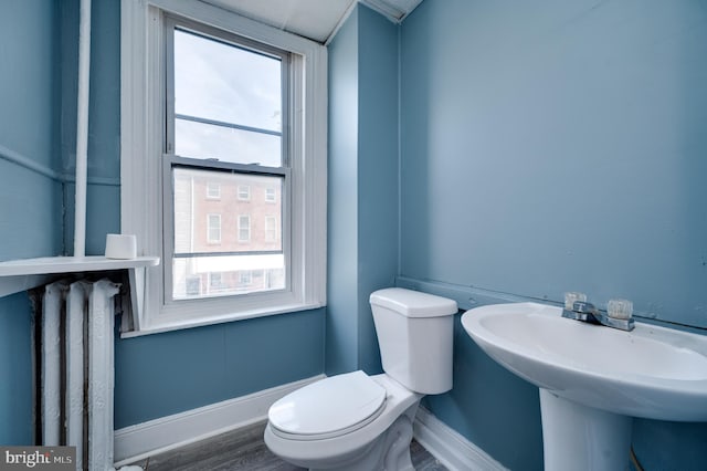 half bathroom with toilet, baseboards, a healthy amount of sunlight, and wood finished floors