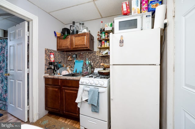 kitchen featuring white appliances, light wood finished floors, decorative backsplash, light countertops, and a drop ceiling