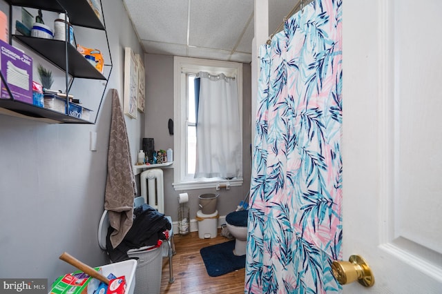 interior space with toilet, wood finished floors, curtained shower, a paneled ceiling, and baseboards