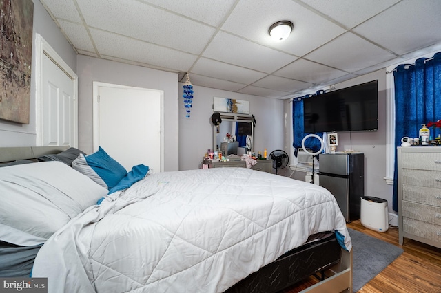 bedroom featuring a paneled ceiling, freestanding refrigerator, and wood finished floors