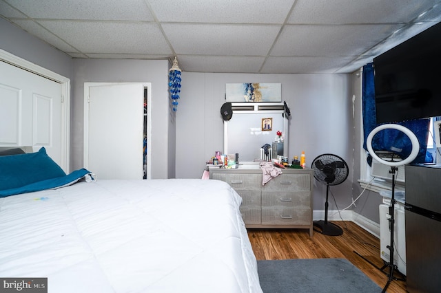 bedroom featuring a paneled ceiling, baseboards, and wood finished floors