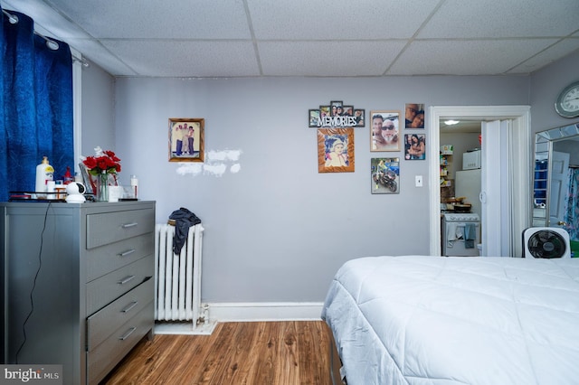 bedroom with a paneled ceiling, wood finished floors, baseboards, and radiator heating unit