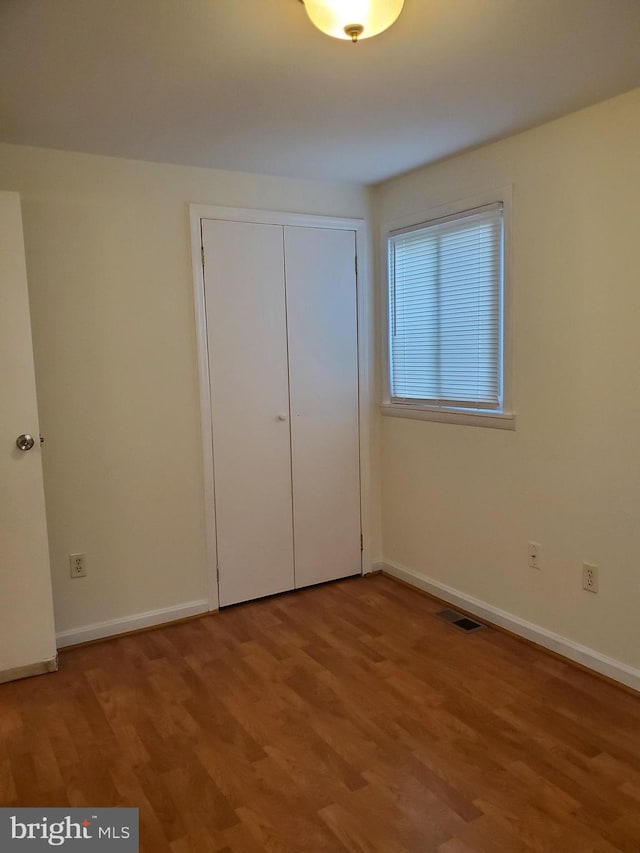 unfurnished bedroom featuring baseboards, visible vents, wood finished floors, and a closet