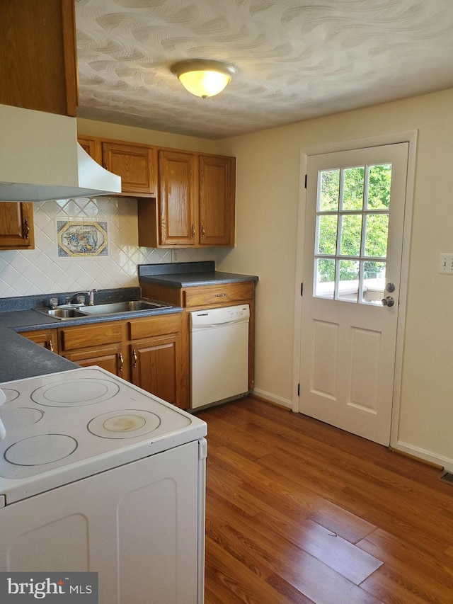 kitchen featuring wood finished floors, dark countertops, white appliances, brown cabinets, and a sink