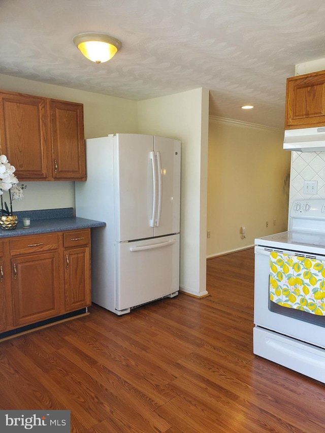 kitchen featuring white appliances, under cabinet range hood, brown cabinetry, and tasteful backsplash