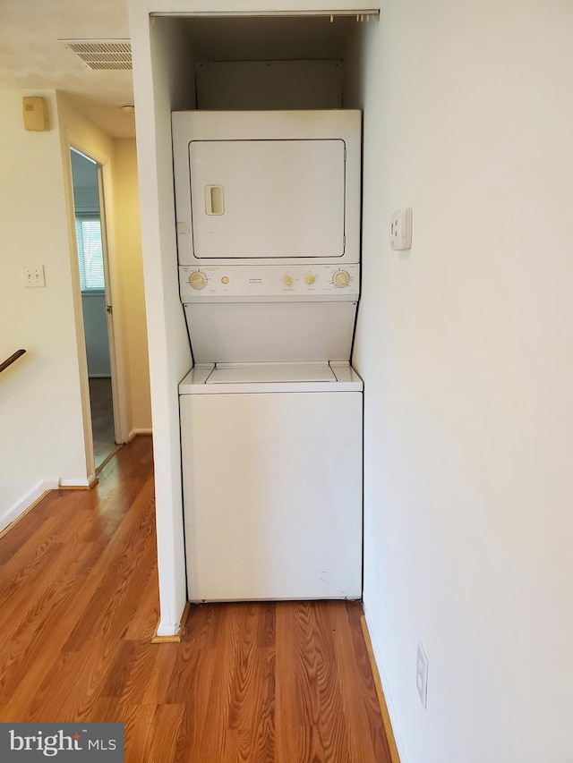 washroom with laundry area, stacked washer / dryer, visible vents, baseboards, and light wood finished floors