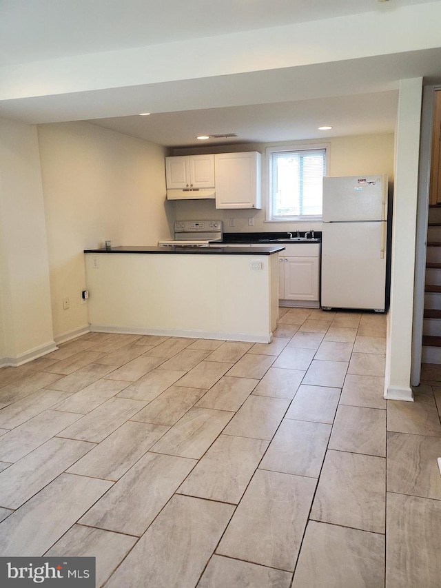 kitchen featuring dark countertops, white cabinetry, under cabinet range hood, recessed lighting, and white appliances
