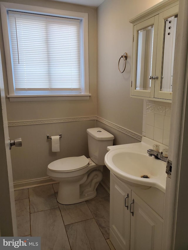 half bathroom with toilet, baseboards, and vanity