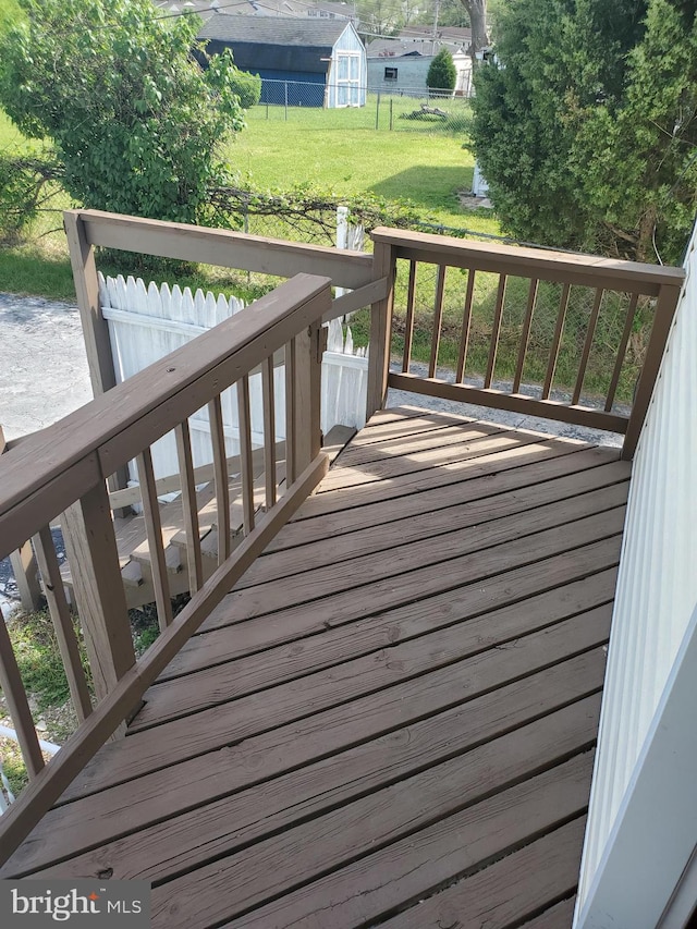wooden deck featuring a lawn, fence, an outbuilding, and a storage shed