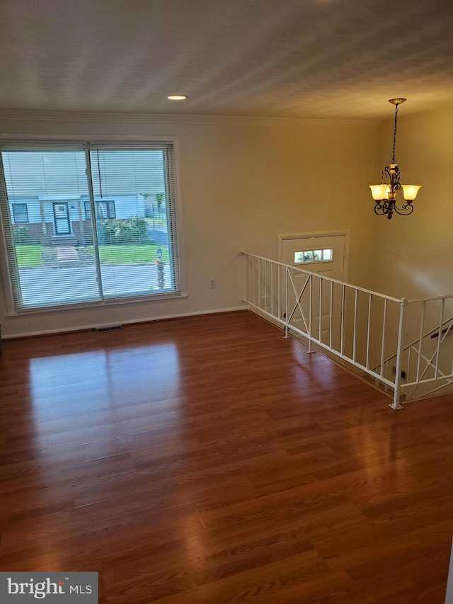 spare room with baseboards, a notable chandelier, wood finished floors, and visible vents