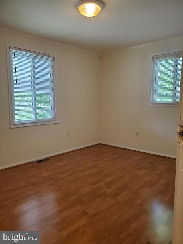 empty room featuring crown molding, wood finished floors, and a healthy amount of sunlight