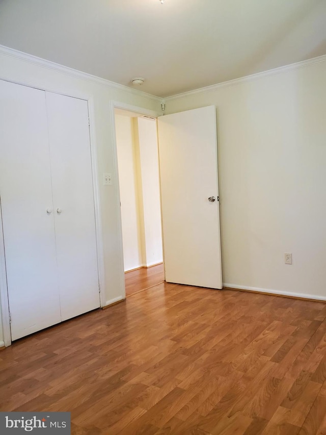 unfurnished bedroom with crown molding, baseboards, a closet, and light wood finished floors