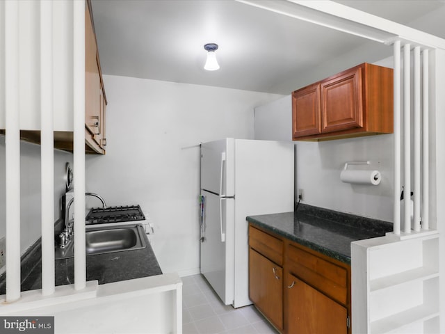 kitchen featuring freestanding refrigerator, brown cabinets, dark countertops, and a sink