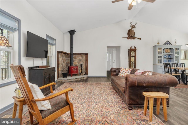 living area with ceiling fan, a wood stove, wood finished floors, and lofted ceiling