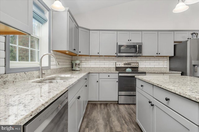 kitchen featuring appliances with stainless steel finishes, tasteful backsplash, light stone countertops, a sink, and dark wood-type flooring